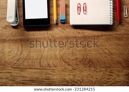 Close up Assorted Office Supplies and Mobile Phone on Wooden Table, Resting at Top Edge with Copy Space Below for Texts.