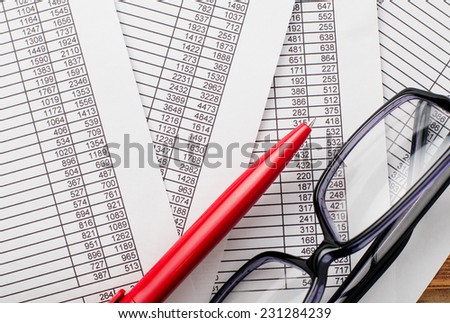 Close up Eyeglasses and Red Ballpoint Pen on Top of Business Documents with Number Prints.
