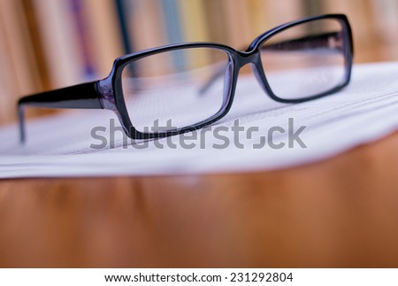 Close up Eyeglasses with Black Frame on Top of White Papers at the Wooden Table at the Office.