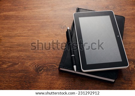 Close up Black Pen and Tablet Gadget on Top of Closed Black Book at the Wooden Table with Copy Space on the Left Side.