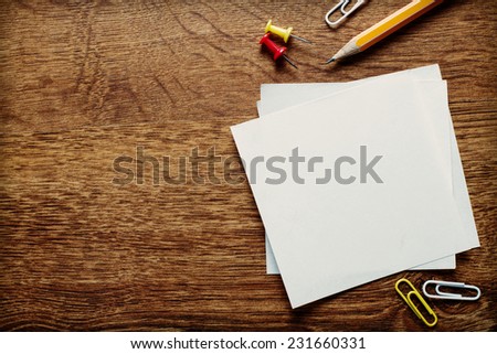 Assorted Office Supplies such as Clean Papers, Pencil, Thumbtacks and Clips on the Wooden Table, Resting at the Bottom Edge with Copy Space Above for Texts.