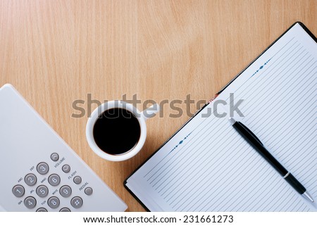 Cup of Black Coffee to Stay Awake in Work on the Table of Telephone Support Officer with Ready Notebook and Pen for Reminders.