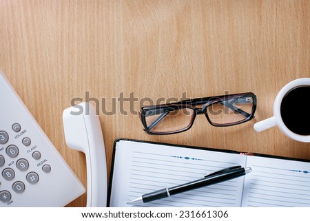 Telephone Operator Stuffs - Eye Wear, Notebook and Pen and a Cup of Coffee on Wooden Desk at the Office.