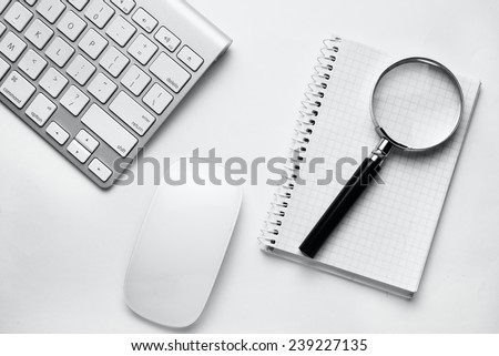 Conceptual image depicting conducting an online search for information with a magnifying glass on a blank notebook alongside a wireless computer mouse and keyboard