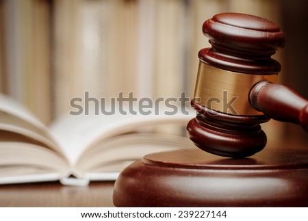 Wooden gavel resting on its end on a wooden table in front of an open law book conceptual of a judge, courtroom and judgements