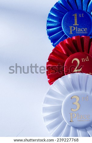 Set of three winners rosettes and ribbons in red, white and blue with gold lettering for 1st, 2nd, and 3rd place on white with copyspace