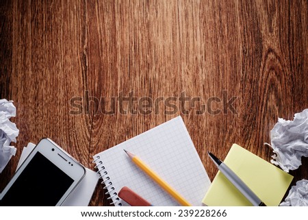 Close up Office Supplies - Phone, Notes, Pen, Pencil, Eraser and Crumpled Papers - on Wooden Table. Captured at the Bottom Border Frame with Copy Space on Top.