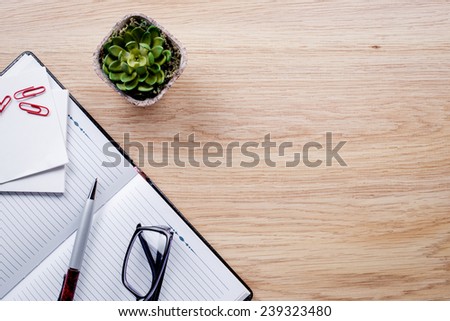 Flower pot, glasses, pen, notebook lie on light brown desktop