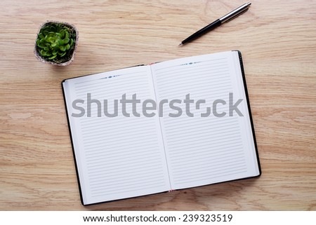 Flower pot, pen, notebook lie on light brown desktop