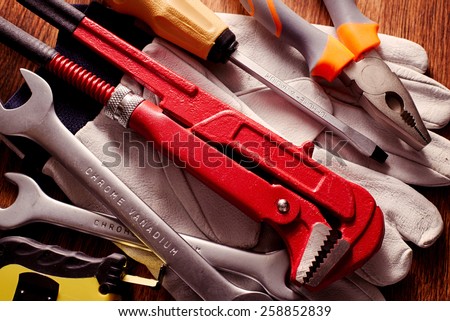 Close up Work Tools like Wrenches, Screw Driver and Pliers on Hand Gloves Placed on Top of a Wooden Table