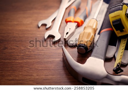 Close up Hand Work Tools on Top of a Wooden Table, Emphasizing Pliers, Hammer, Screw Drivers and Gloves.