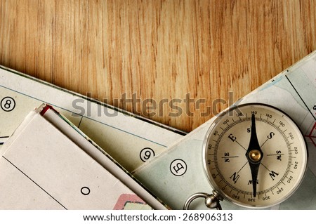 Close up Vintage Compass Instrument on Top of a Wooden Table with Folded Maps, Captured in High Angle View.