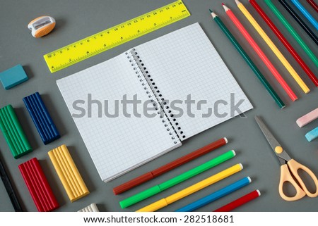 High Angle View of Colorful School Supplies Organized by Type Around Note Book Open to Blank Page Arranged on Grey Desk