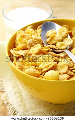 milk in a glass cup and corn flakes in a yellow bowl