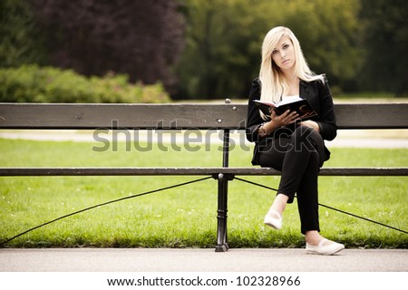 cute blonde sitting in the park reading book. Front view