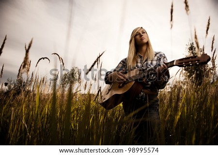 Young blonde girl with the guitar on a meadow