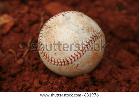 One Single used baseball in red dirt on basebal field`