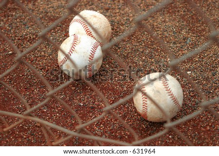 Three Used Baseballs on Red Dirt behind a Chain Link Fence