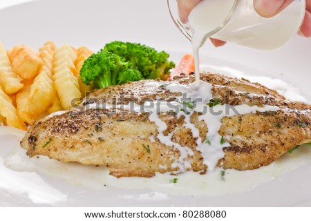 fish steak with fries and salad hand pours milk into the fish on white plate .