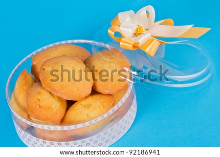 Small shell-shaped tea cakes in Christmas package  and yellow  ribbon Isolated on blue background.