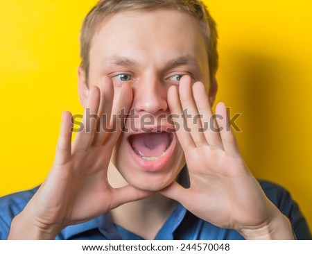 Two hands covering her mouth on the sides show a loud cry. young guy on a yellow background. Photo. Men loudly calling someone.