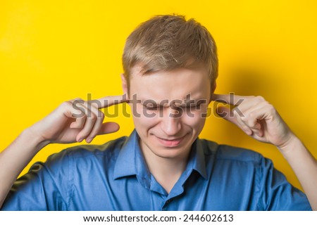 Blond young man shows he does not want to hear from you. Fingers in his ears. gesture. Close portrait. Isolated yellow background. photo