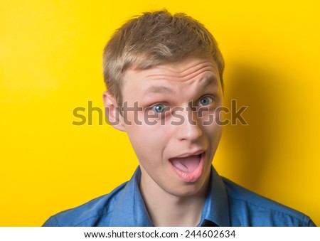 Young, serious, blond man in a blue shirt on a yellow background. How glad I am to see you. smile. Gesture. Photo Shoot.