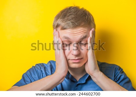 Portrait of young naked man closed face by two hands isolated on yellow background