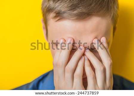 Young man in a blue shirt on a yellow background. showing fatigue, sleepy, sleepy, closes his eyes with his hands. gesture. photo shoot