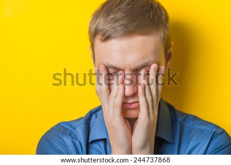 Blond young man thinks thinks. head resting on her hand, looking into the camera. Gesture. Isolated yellow background.