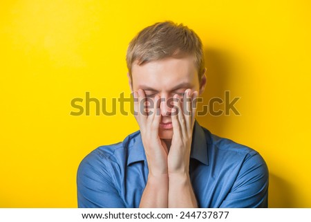 Blond young man thinks thinks. head resting on her hand, looking into the camera. Gesture. Isolated yellow background.