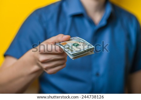 Dollars. A young man close-up in a blue shirt on a yellow background, gives or takes money. Holds money in hands. . Photos
