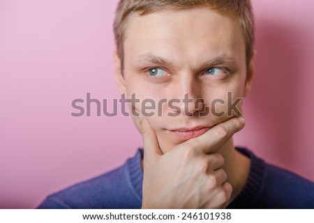 Blond young man thinks thinks. head resting on her hand, looking into the camera. Gesture.