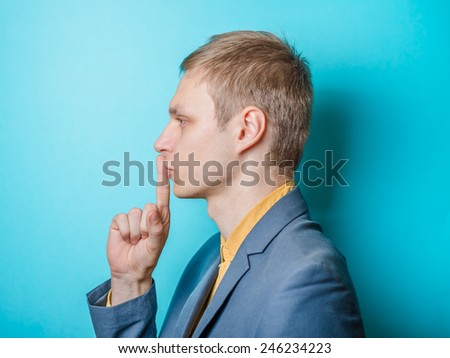 Closeup portrait of young man, student, coach, trainer, worker placing finger on lips shhh, asking to be quiet