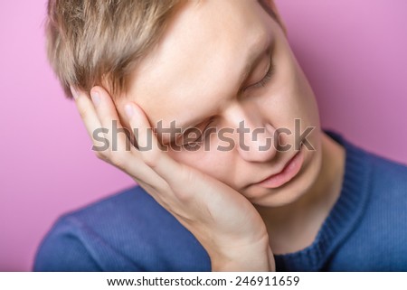 Young Man wants to sleep. Put his head in his hands. Gesture. On a purple background.