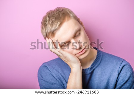 Young Man wants to sleep. Put his head in his hands. Gesture. On a purple background.