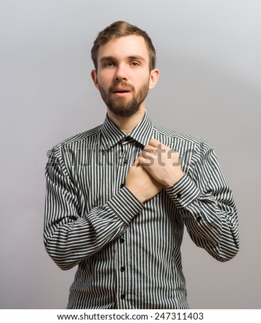 Young handsome man upset keeps his heart, hands on heart. Gesture. On a gray background