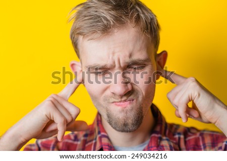 Blond young man shows he does not want to hear from you. Fingers in his ears. gesture. Close portrait. Isolated yellow background. photo