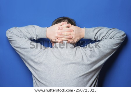 Teenager holds hands behind head on white background
