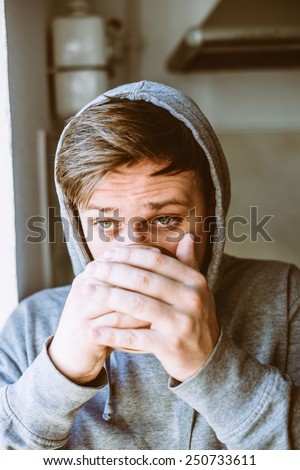 Relaxed young man in hood drinking coffee at home, near the window