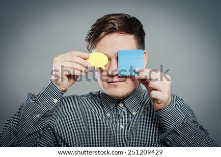 Closeup portrait of young man with a piece of paper covering his eyes on gray background