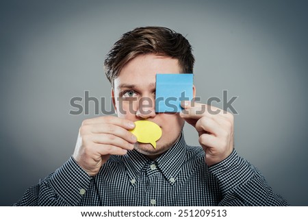 Closeup portrait of young man with a piece of paper covering his mouth and eyes on gray background