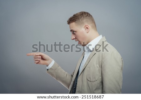 Closeup side view portrait of young man, laughing, pointing with finger at someone or something. Positive human face expressions, emotions, feelings, attitude, approach