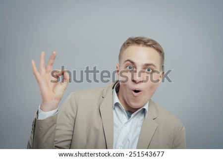 Gesturing OK sign. Cheerful young man in shirt gesturing OK sign while standing against grey background