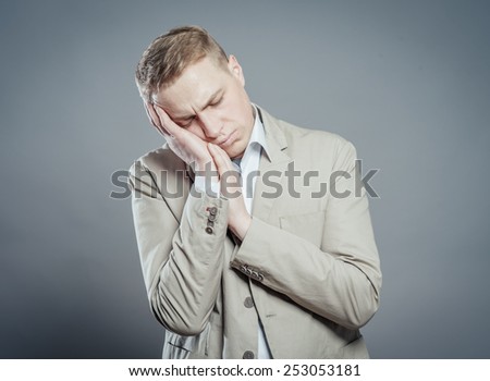A young man close-up in a suit on a gray background, fall asleep. The guy wants to sleep. Gesture. Photos