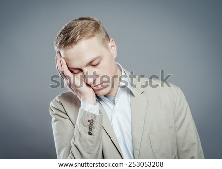 A young man close-up in a suit on a gray background, fall asleep. The guy wants to sleep. Gesture. Photos