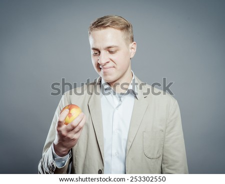 Cheerful beautiful man eating apple, isolated over gray background