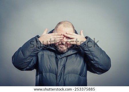 Close-up portrait of a young man covering face with his hands with enough space to look through the isolated gray background. Negative human emotions facial expression feelings, reactions.
