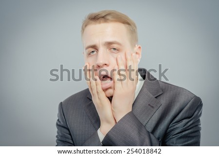 Portrait of young desperate businessman pulling his face down isolated on gray