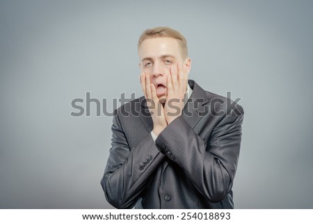 Portrait of young desperate businessman pulling his face down isolated on gray